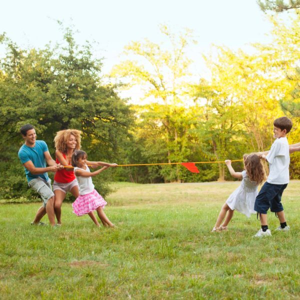 Two Families having fun playing tug of wars outdoors, after barbecue party. One Caucasian family and other mixed race family.